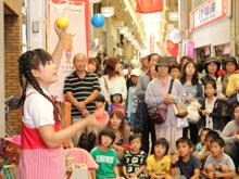大道芸で3色のボールのジャグリングを披露している女性を沢山の人達が見にきている写真
