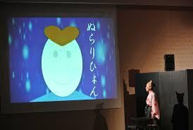 大きなスクリーンに映し出されたぬらりひょんと書かれたイラストの右側に、男性が立っている一場面の写真