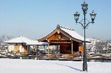 公園内の能舞台の屋根や地面に雪が積もっている写真