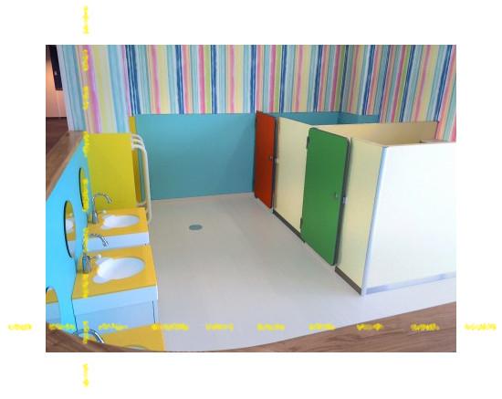 赤色と緑色のトイレのドアや、熊の顔の形をした洗面台や丸い鏡が設置されている子供用トイレ全体を写した写真