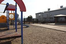 左側に遊具が設置され、舗装された歩道の奥に東屋が見える公園の写真