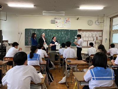 リズモー学生が高田中学校教室内で生徒のプレゼンを聞いている様子