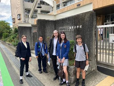 リズモー学生たちが菅原小学校を訪問し、正門の前で記念撮影している様子