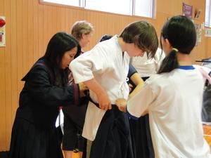 制服や体操服を着た女子中学生に手伝ってもらいながら道着を着ているリズモー市の男子学生の写真