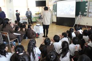 スカイプの画面が映し出されたスクリーンをみている陵西小学校6年生の写真