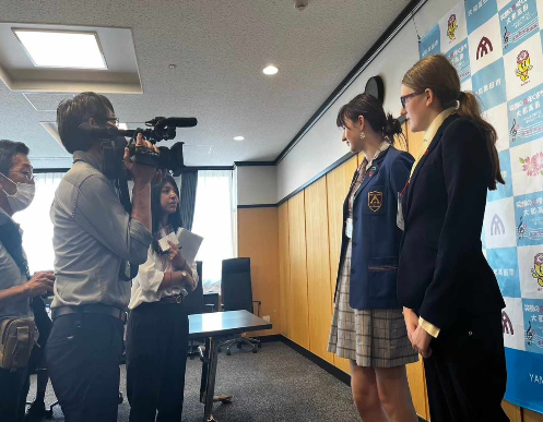 市長応接室で2人のリズモア市の学生が2人の取材者に向いていて、取材を受けている様子、1人の取材者が大きなカメラを持っている様子、取材者の横に通訳者がいる