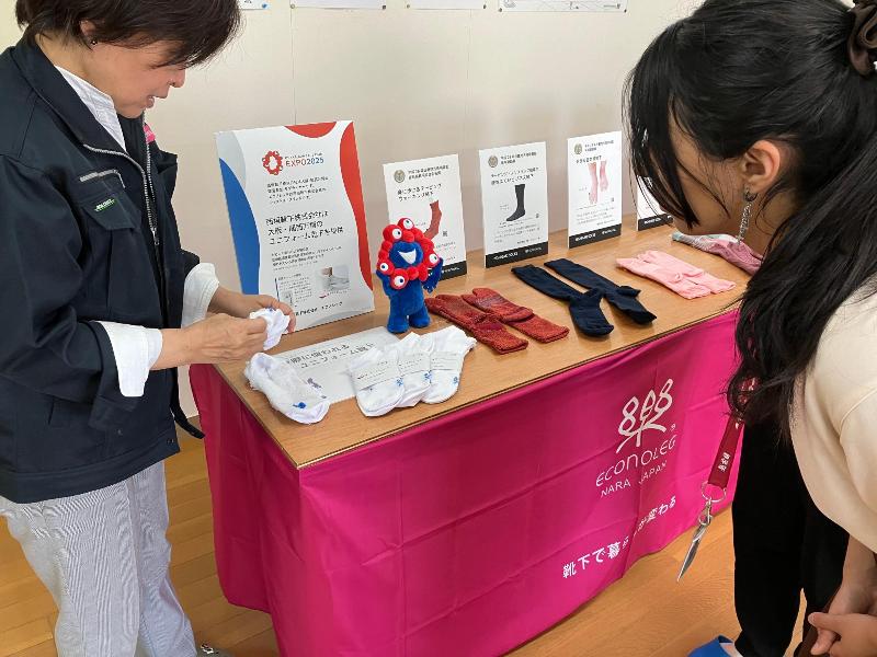 テーブルに靴下がおいてあります。テーブルの前に女性が2人が立っていて、喋っている様子です。