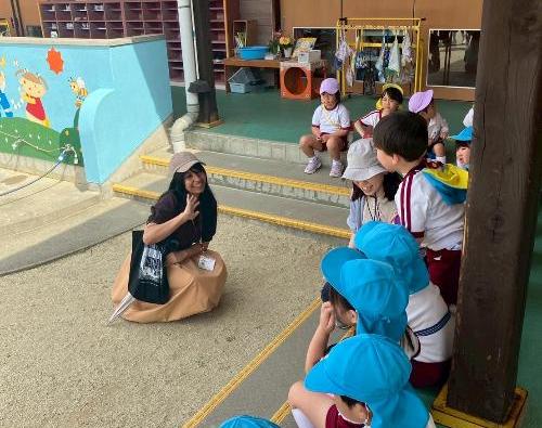 子供たちの前に、1人の女性が子供に手を振って笑っている様子