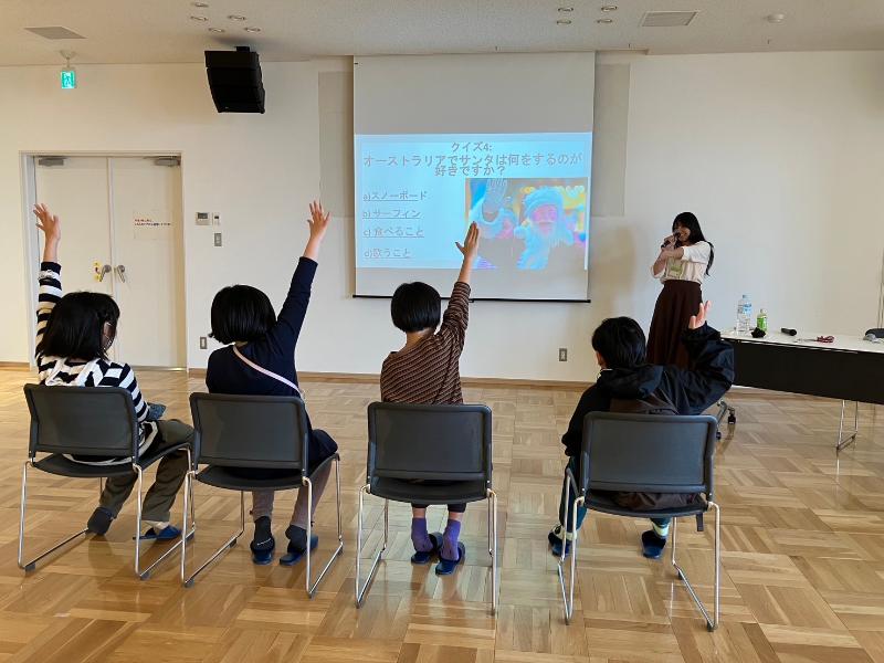 4人の子供たちは円の形で床に座っている様子。子供たちの前にプロジェクターがあって、プレゼンの内容が映っています。