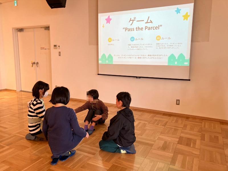 4人の子供たちは円の形で床に座っている様子。子供たちの前にプロジェクターがあって、プレゼンの内容が映っています。