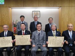 授賞式で前列で表彰された3名が賞状を持ち関係者の人達が5名参加しての記念撮影をしている写真