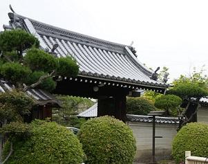 入り口付近に手入れされた植木がある、本瓦葺きの屋根の名称寺の門の写真