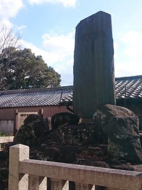 高田城址の碑が石で囲まれ、後方に瓦屋根の建物が建っている写真