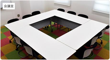 4つの長テーブルをロの字に設置し、椅子が3脚ずつ置いてある会議室の写真