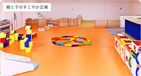 左壁側に小さなピアノや、黄色や赤色などのカラフルな色の遊具が設置されている親と子のすこやか広場の写真