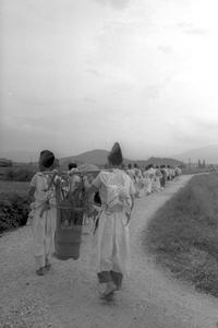奥まで続くあぜ道を、修験者たちが一列になって練り歩いている白黒写真