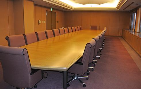細長いテーブルの両脇や両端に椅子が設置されている会議室の写真