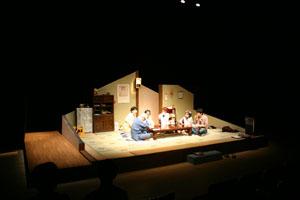 居間を舞台に6名の家族が座卓を囲んで座っている一場面の写真