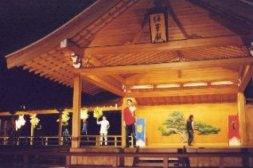 能舞台の上で、赤色の服を着た男性が演技を行っている一場面の写真