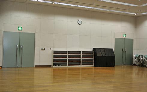壁に靴箱やピアノがあり、両端に出入口が設けられているリハーサル室の写真