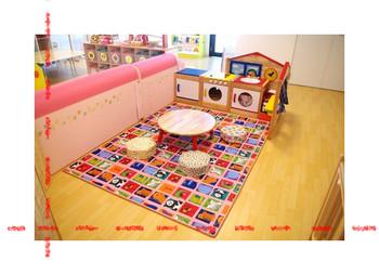 丸い座卓の周りに丸いクッションが置いてあり、奥にままごとキッチンがある託児室内の写真