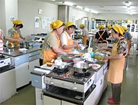 黄色のエプロンと三角巾をした食生活改善推進員の方々が調理台で料理を作っている写真