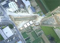 道路の右側の、三角形や台形などの形をした遺跡調査跡を上空から撮影した写真
