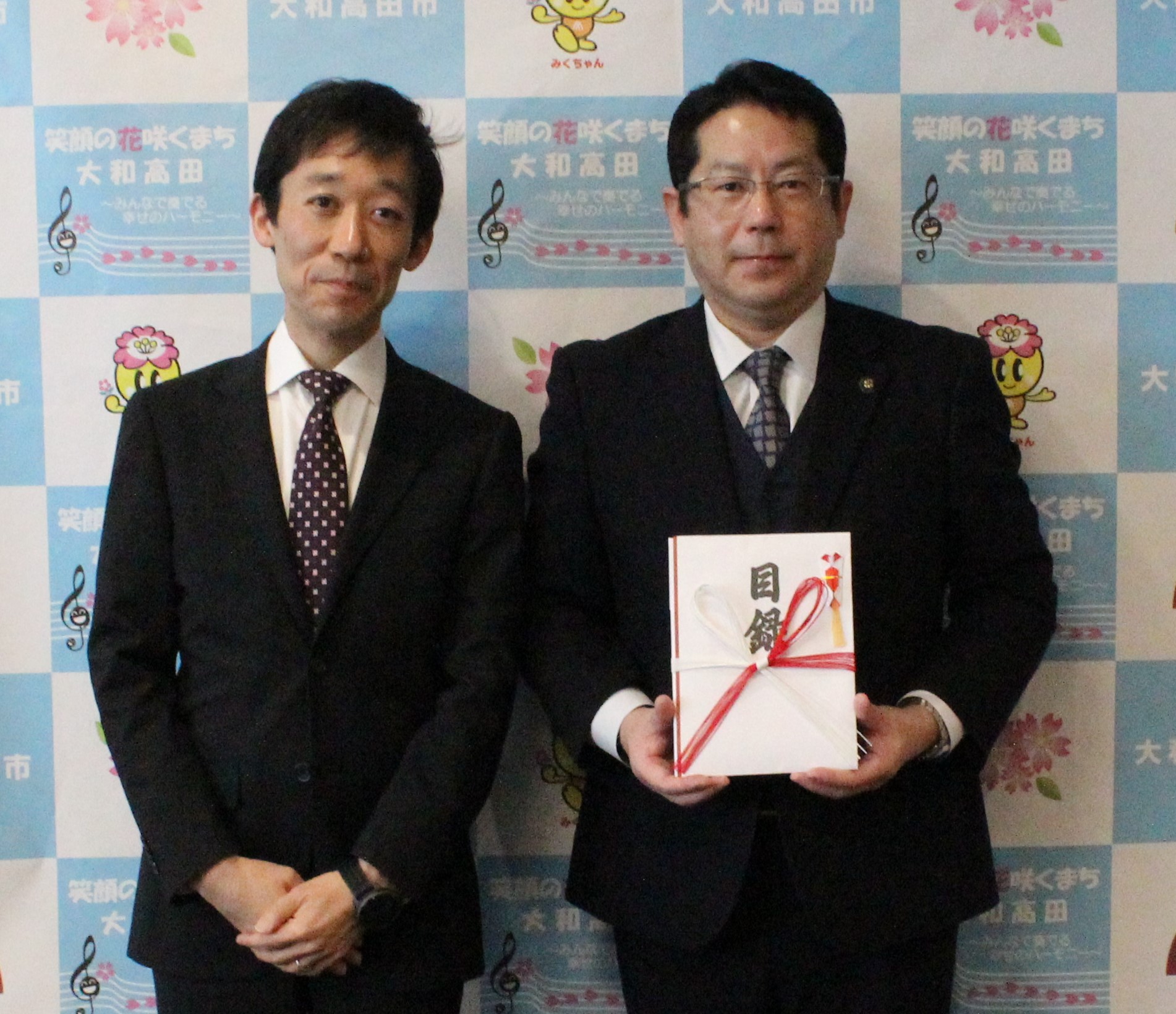 寄附目録贈呈式の模様（ダイヤモンド・リアルティ・マネジメント株式会社 丸山経理部長(左)と堀内市長(右)）