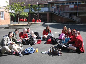 リズモー市の女子学生7人と、日本の学生2人が半円を描いて地面に座り笑顔で写っている写真