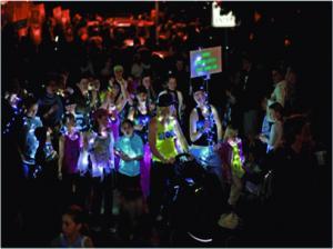 洋服にいろいろな電球をつけ光っている人達のパレードの写真