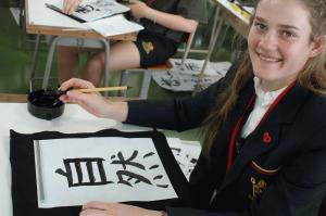 リズモー市の女子学生が書道で「自然」と書き笑顔でカメラを見ている写真