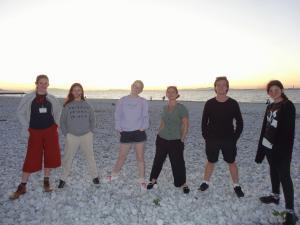 海岸でみんなで両足を広げてポケットに手を入れポーズを決めて記念撮影をしているリズモー市からの6名の学生の写真