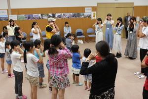 派遣学生と子供達が円になり耳に両人差し指をあてている写真