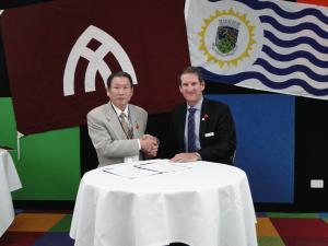 姉妹都市提携盟約の再確認書の署名後、握手をしている日本人男性とリズモー市の担当の方の写真