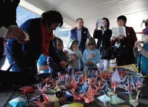 いろいろな柄の折り紙で作られた折鶴を手に取る子供達やそれをスマートフォンで撮影している参加者達の写真