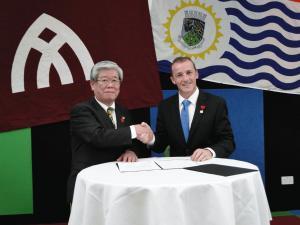 姉妹都市提携盟約の再確認書の署名後、握手をしている眼鏡をかけた白髪の日本人男性とリズモー市の担当の方の写真