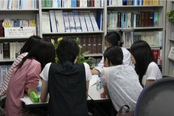 6人の女子学生がテーブルを囲んで高田紹介パンフレットを作成している様子を後ろから写した写真