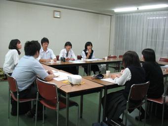 ロの字に並べられた長机に6名の学生と男性が座り派遣学生研修が行われている写真