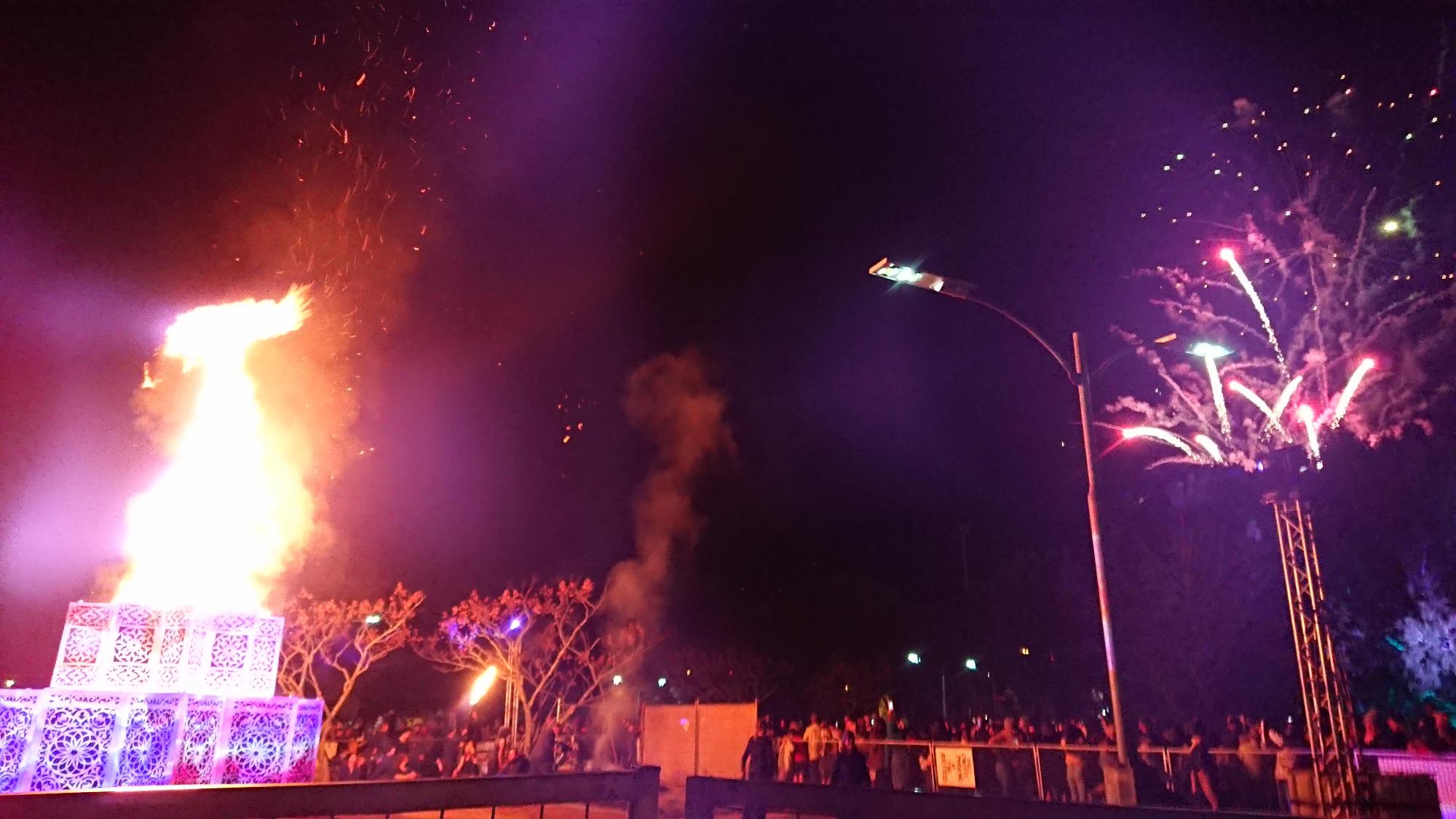 パレードに参加したたくさんの人たちが夜空の中集まって右側の打ち上げ花火を見ている写真