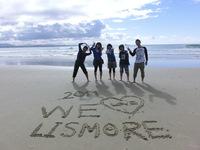 「2011 WE LOVE LISMORE」と書かれた砂浜で5名が記念撮影をしている写真