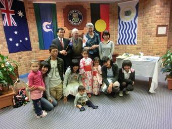 オーストラリアの旗などが掲げられた室内で日本人学生とリズモー市の関係者と子供達が笑顔で記念撮影をしている写真