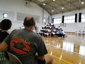 体育館で4段の大きな人間ピラミッドを作っている小学生達を見ているリズモー市の学生たちの写真