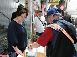 関係者の女性の前にある募金箱に募金する男性の写真