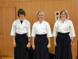 剣道の道着を着、左手に木刀を持って笑顔で記念撮影をしているリズモー市の学生3人の写真