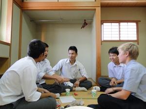 あぐらを組み高田商業高等学校の男子生徒と話をしている外国人男性の写真