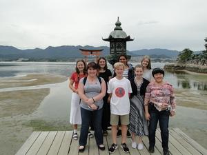 リズモー市の学生7名と引率の先生が遠目に海に浮かぶ鳥居をバックに記念撮影をしている写真
