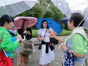 傘をさしながらピースボランティアの人の話を聞いている外人の女性2名の写真
