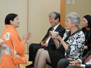 オレンジ色の着物を着た女性が湯呑を持って椅子に座っているジェニー・ドウェル市長に話をしている様子の写真
