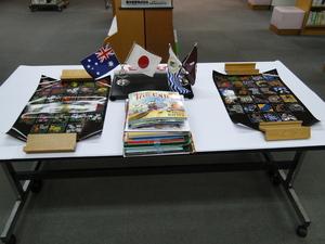 机の上にオーストラリアと日本の小さい国旗、リズモー市と大和高田市の小さな旗、2枚のポスターと複数の本が重ねて置かれている写真