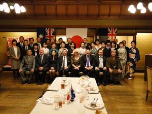 日本とオーストラリアの国旗が飾られた部屋の夕食会で参加者が記念撮影をしている写真